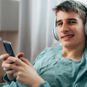 Jongen met koptelefoon in zetel en gsm in de hand.
